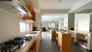 Una cocina moderna con estufa a gas, cafetera y lavabo. Se observa un comedor con mesa y sillas al fondo.