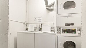 A laundry area with stacked washing machines and dryers, a vent above the dryers, and a small window on the top right. - Cosy Studio With City Views (Sydney)