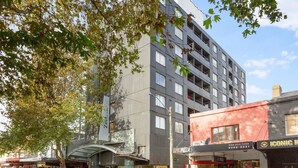 A multi-story building with a modern design, featuring a large glass facade and a red storefront with a pizza restaurant. - Cosy Studio With City Views (Sydney)