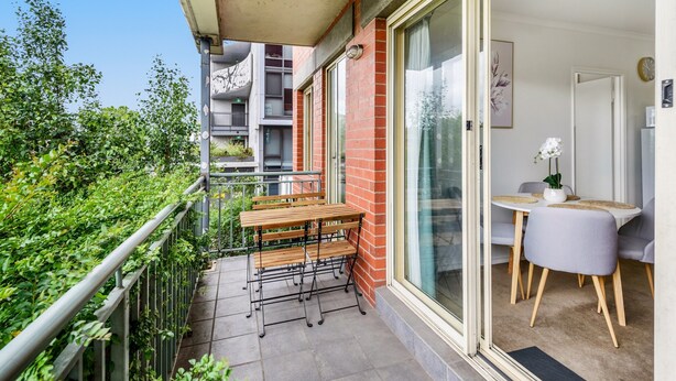 A balcony with a table and chairs, a small dining area with a table and chairs, and a view of greenery and buildings in the background. - Chic 2-bed Apartment Near Albert Park (Melbourne)