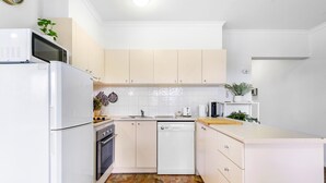 A compact kitchen with white cabinets, a dishwasher, a microwave, and a stove. - Chic 2-bed Apartment Near Albert Park (Melbourne)