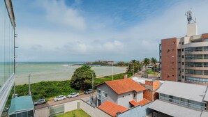 A coastal view with a building featuring a red-tiled roof, a parking area, and a clear view of the sea. - Apt w/ Balcony and sea View in Guarapari Cmd0311 (Guarapari)