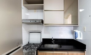 Una cocina con estufa a gas, lavamanos y cafetera.