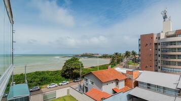 A coastal view with a building featuring a red-tiled roof, a parking area, and a clear view of the sea.