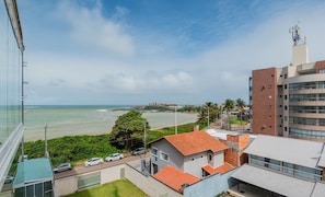 Vista costera con un edificio de techo de tejas rojas, un estacionamiento y una vista despejada del mar.