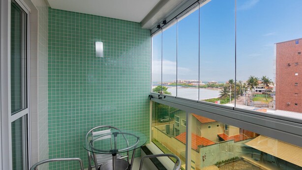 Un balcon avec une table et des chaises en verre, un mur recouvert de carreaux verts et une vue sur des bâtiments et une étendue d’eau.