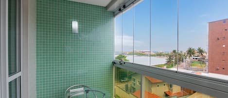 Un balcón con una mesa y sillas de vidrio, un muro de azulejos verdes y vistas a edificios y una masa de agua.
