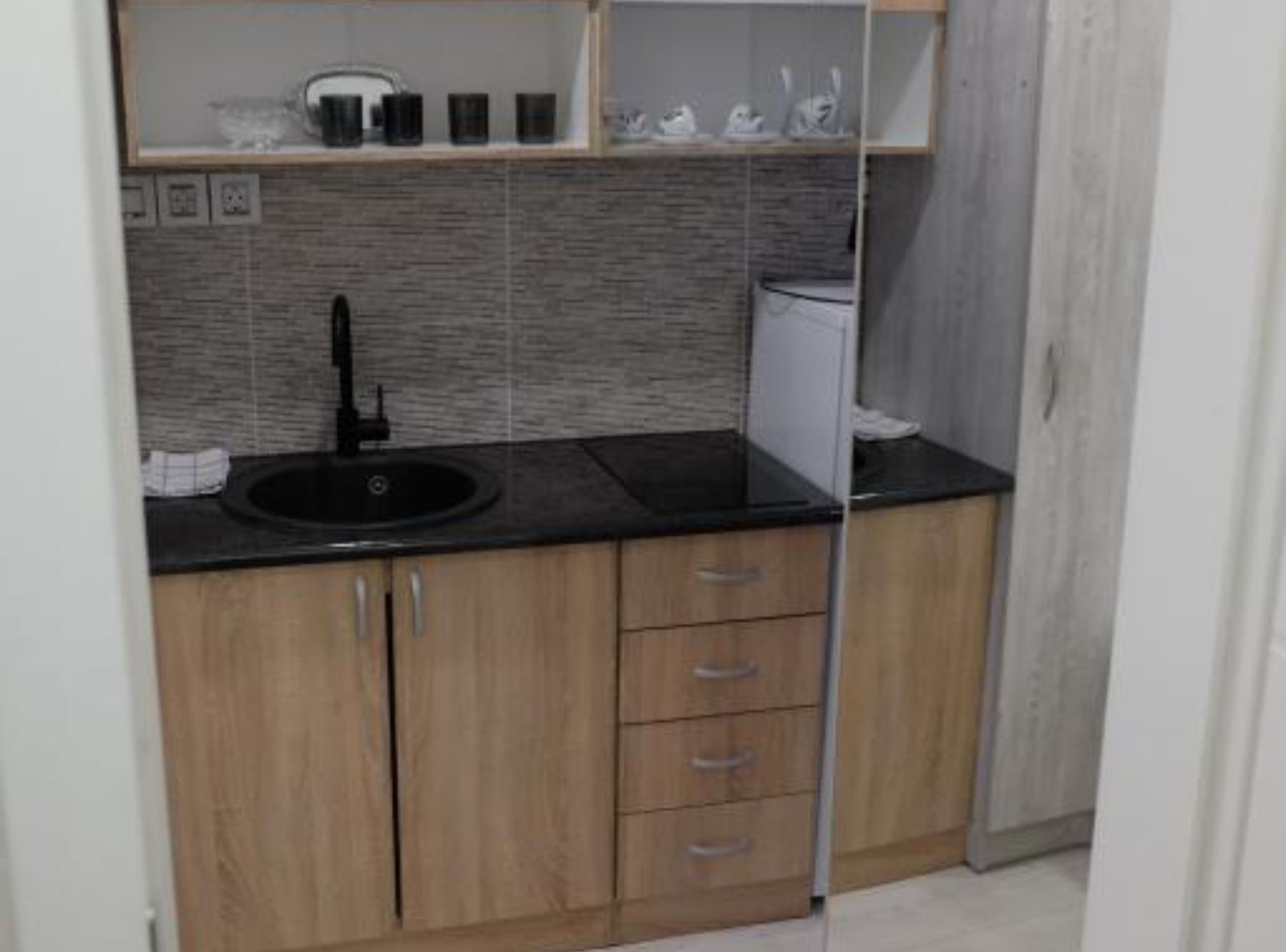 A small kitchenette with a black countertop, a sink, and wooden cabinets.
