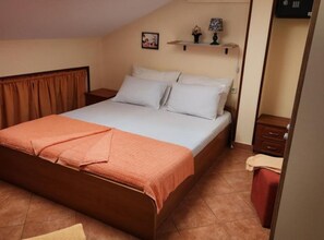 Een slaapkamer met een bed, een nachtkastje, een plank met decoratieve spullen en een rode stoel.