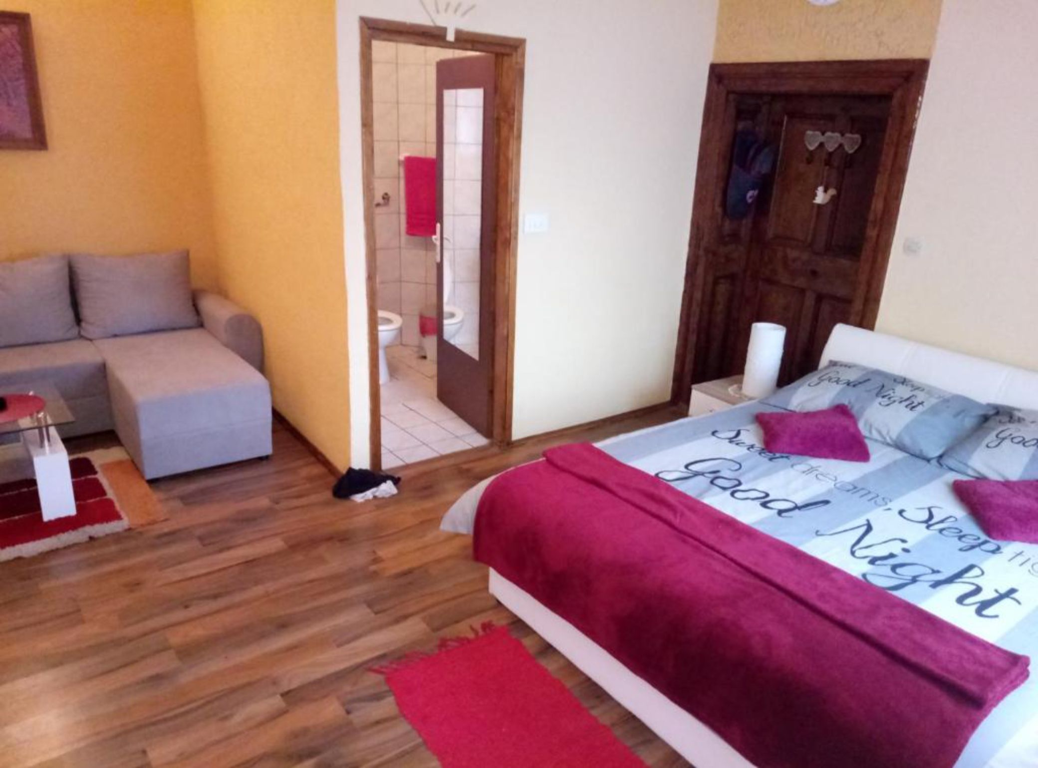 Un dormitorio con cama, sofá, piso de madera y una puerta que da a un baño.
