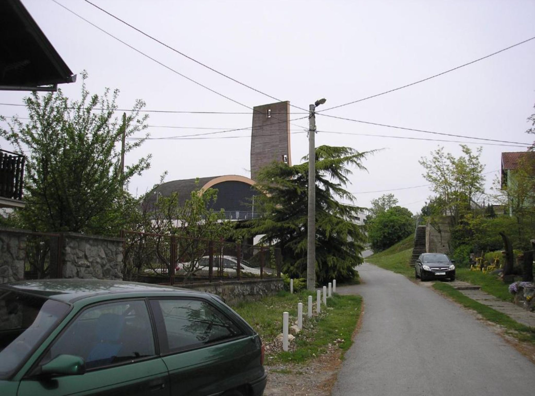A narrow road with a stone wall on one side and a building with a dome and a tall chimney on the other.