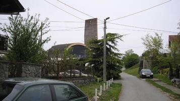 A narrow road with a stone wall on one side and a building with a dome and a tall chimney on the other.
