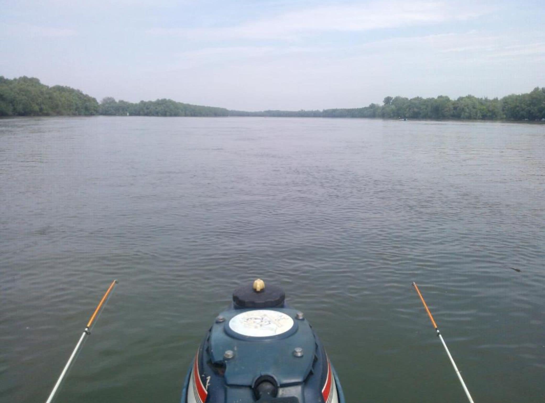 A boat on a calm river with a forested bank on both sides.