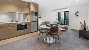 Une cuisine moderne dotée d’appareils électroménagers intégrés, un coin repas avec une table ronde et des chaises, et une vue sur la ville grâce à de grandes fenêtres.
