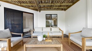 Ein modernes Wohnzimmer mit Holzboden, einem weißen Sofa, zwei Holzsesseln, einem Couchtisch und einem großen Fenster mit Aussicht.