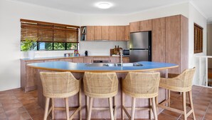 Eine moderne Küche mit Holzschränken, einem Edelstahlkühlschrank und einer blauen Kochinsel mit vier Korbstühlen.