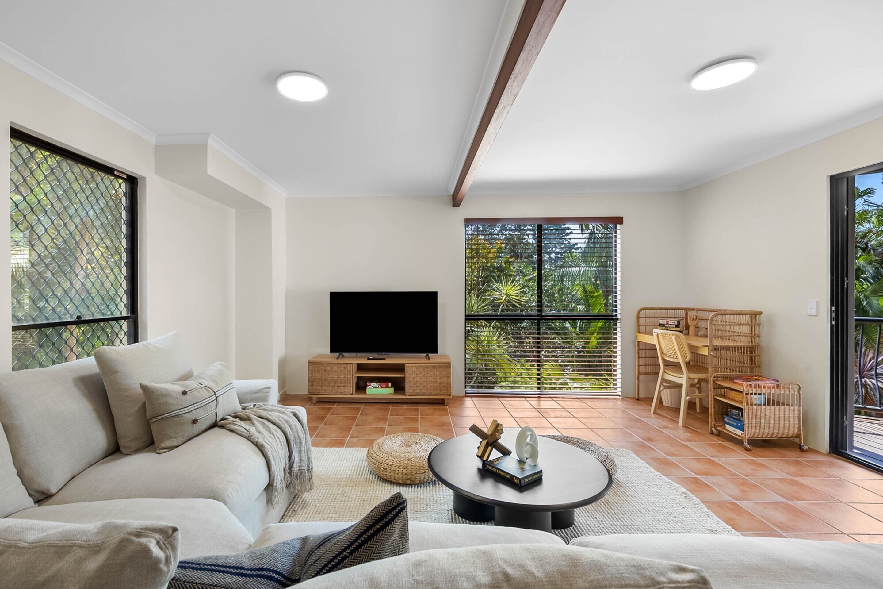 Un salon moderne avec un canapé, une table basse et un meuble pour la télévision. Il y a un balcon avec vue sur la verdure.