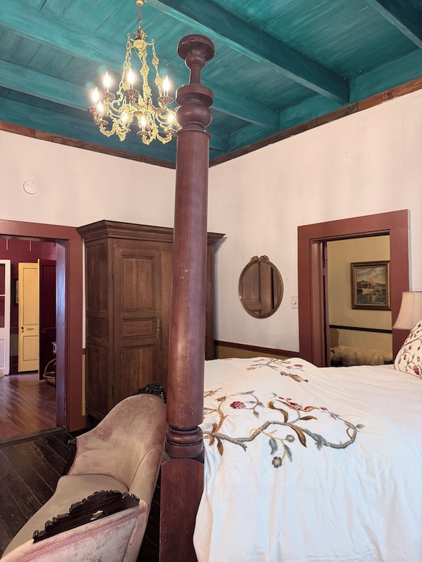 A bedroom with a four-poster bed, a chandelier, wooden furniture, and a large mirror.