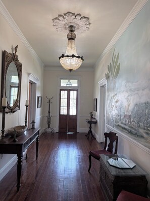 A spacious hallway with a chandelier, a large mirror, and a painting on the wall.