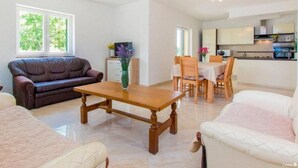 A living room with a sofa, a coffee table, and a dining area with chairs and a table. There is a kitchen in the background. - Villa Dalmacija (Drnis)