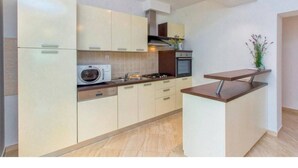 A modern kitchen with white cabinetry, a built-in microwave, a stove, and a small island with a countertop. - Villa Dalmacija (Drnis)