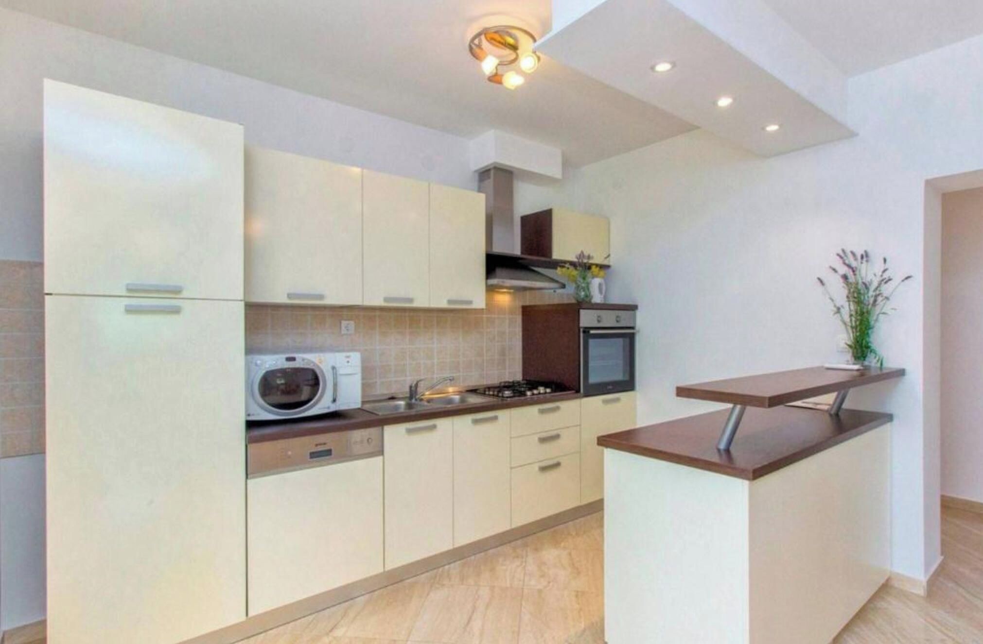 A modern kitchen with white cabinetry, a built-in microwave, a stove, and a small island with a countertop.