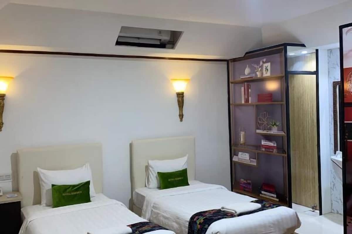 A hotel room with two beds, a nightstand, a bookshelf, and wall-mounted lamps.