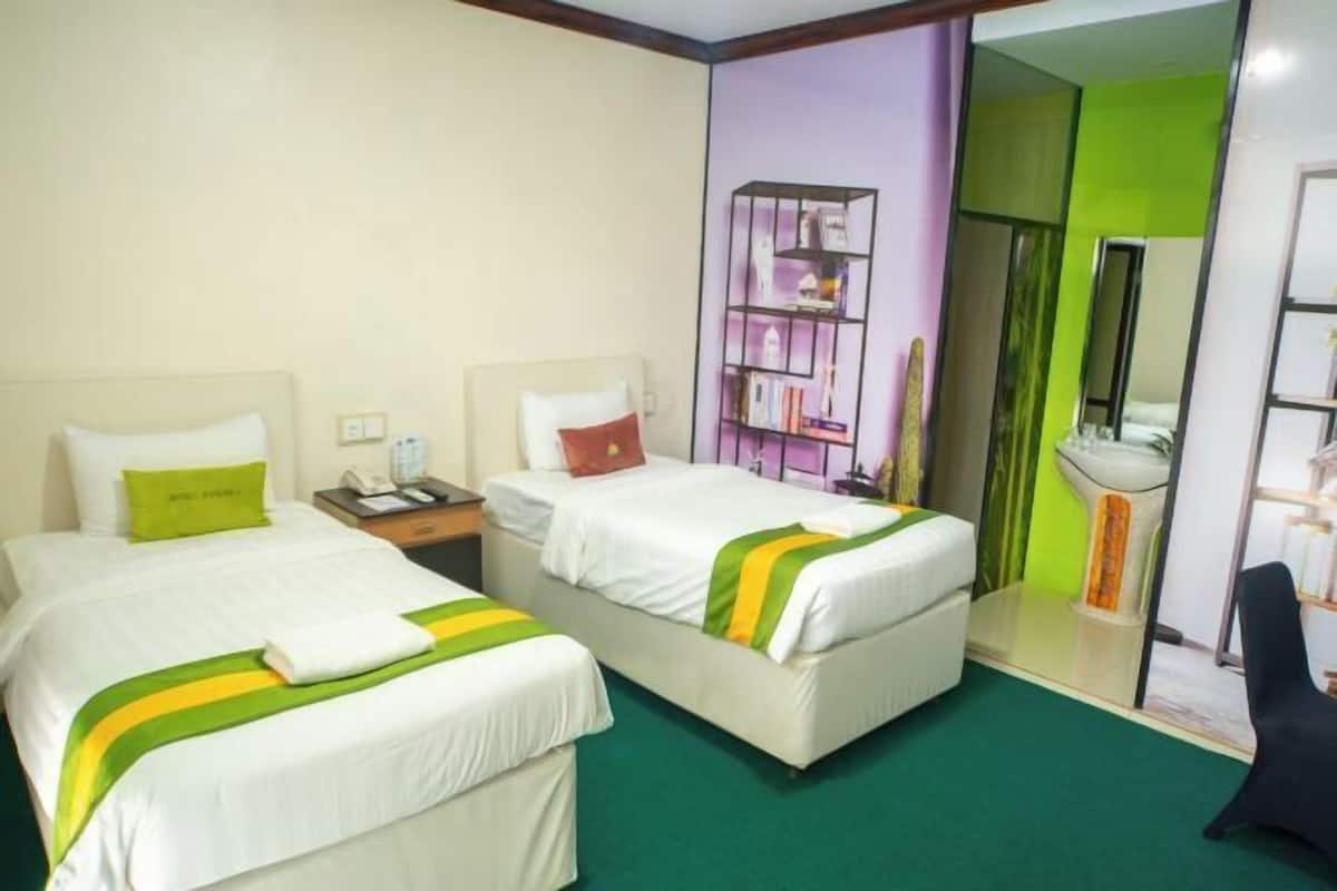 A hotel room with two beds, a nightstand, a bookshelf, a mirror, and a bathroom visible through an open door.