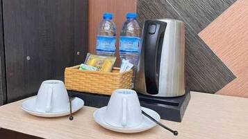 A hotel room with a coffee maker, two cups, a basket with water bottles, and a tray.