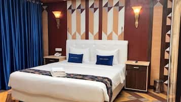 Quarto de hotel com uma cama grande, duas mesas de cabeceira, um criado-mudo e uma luminária fixada na parede, além de um design de parede estampado.