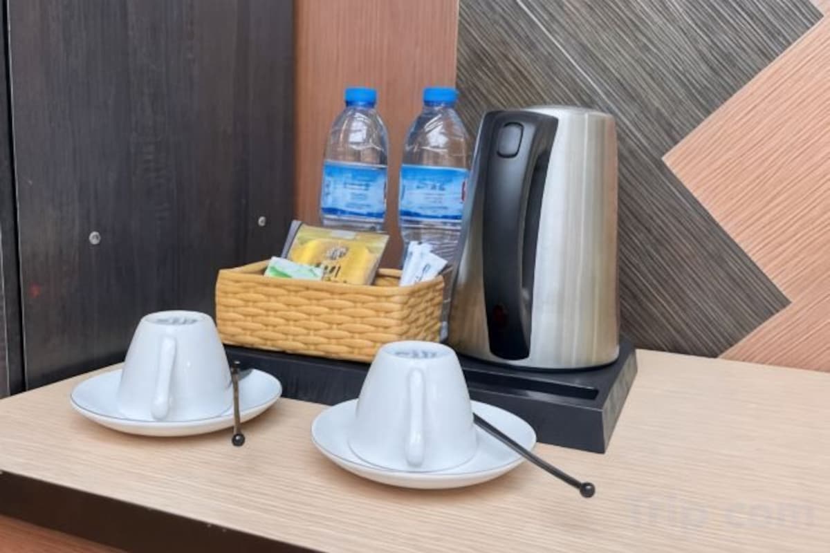 A hotel room with a wooden table, two white teapots with saucers, a kettle, a basket with bottled water, and a telephone.