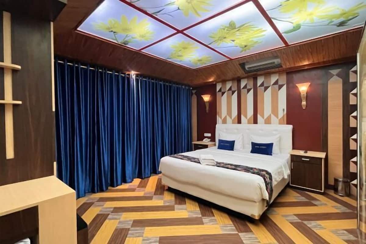 A hotel room with a bed, a desk, a blue curtain, a patterned floor, and a ceiling with a floral design.