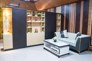 A modern living room with a sofa, coffee table, and built-in shelving with decorative items. - Qubah 9 Hotel kendari (Kambu)
