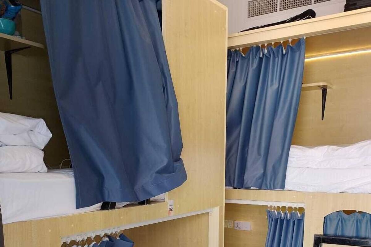 A bunk bed room with blue curtains, a small shelf with toiletries, and a bed with white bedding.