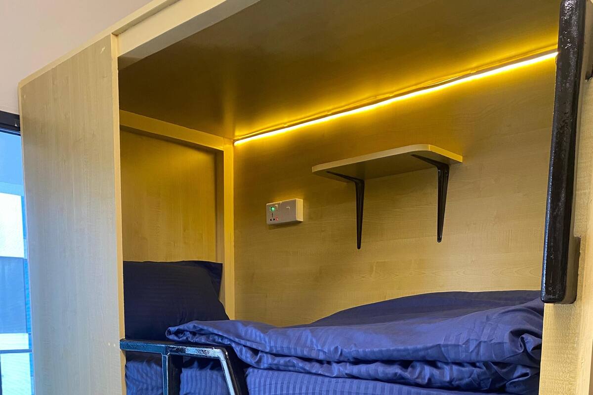 A bunk bed with a desk and a shelf, a power outlet, and a window.