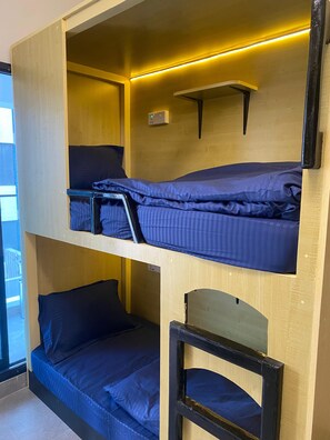A bunk bed with a desk and a shelf, a power outlet, and a window.