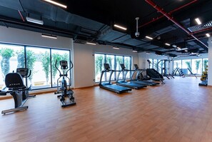 A spacious gym with cardio machines, weight stations, and large windows offering natural light.