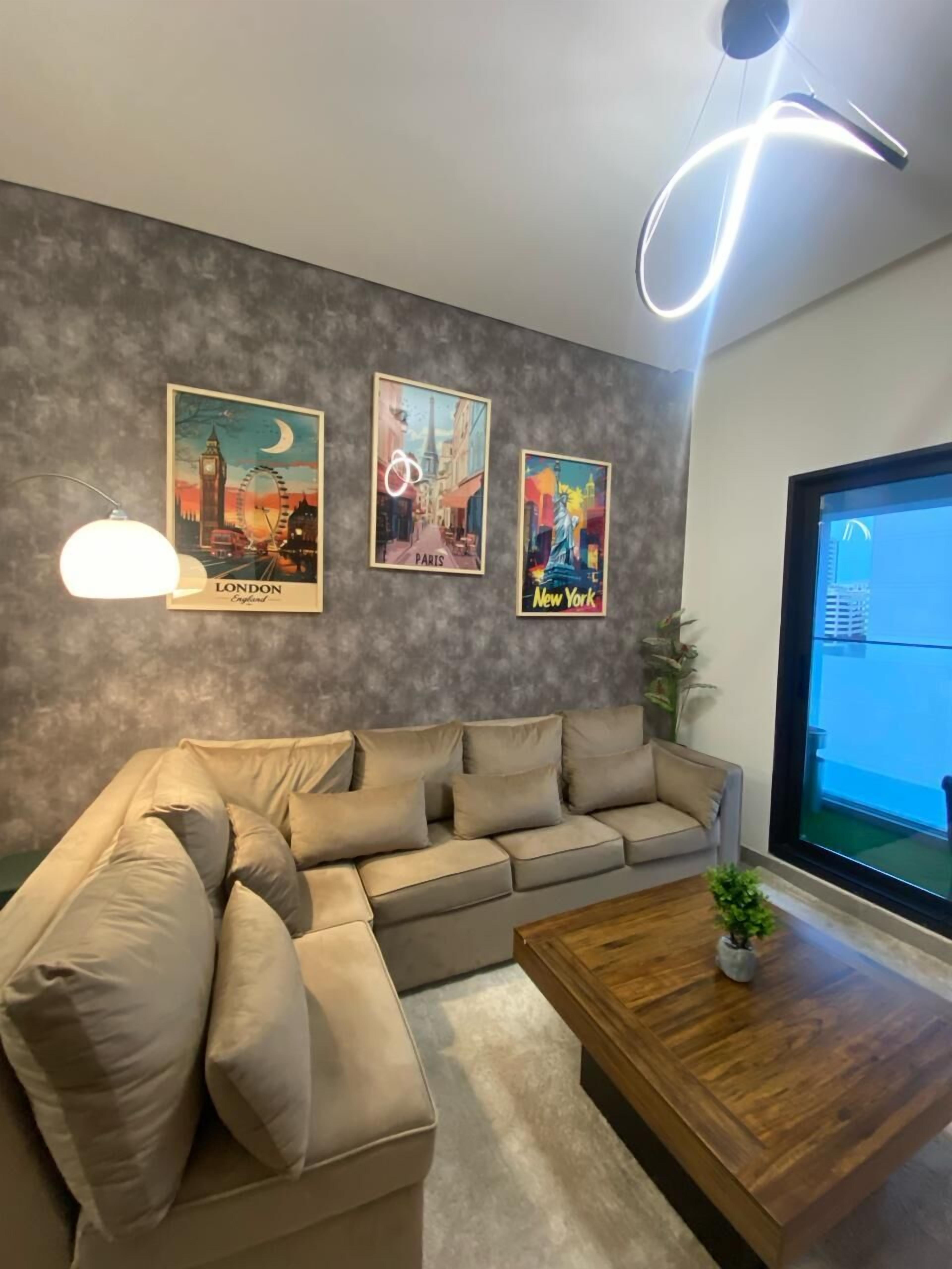 A modern living room with a beige sectional sofa, a wooden coffee table, and three framed posters of London, Paris, and New York.
