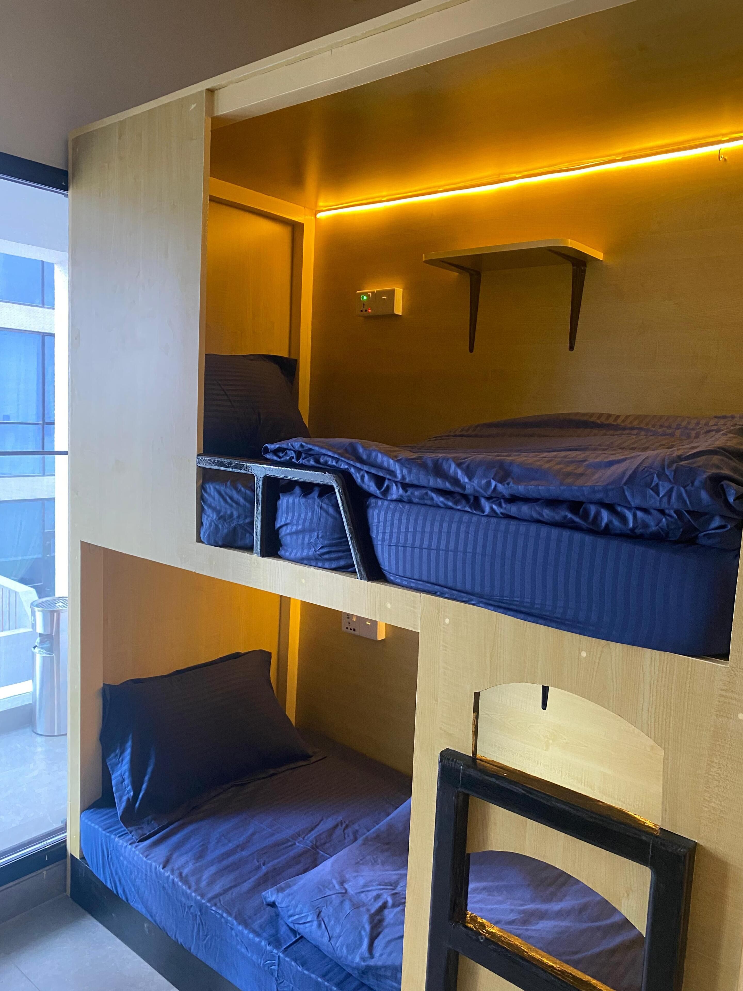 Une chambre avec un lit superposé, une tête de lit en bois, une petite étagère et une fenêtre.
