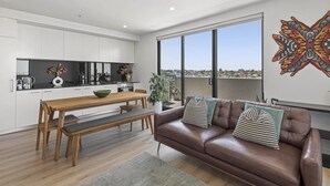 A modern living space with a dining area, a brown leather sofa, and a large window offering a city view. - Bright City-view Retreat in the Heart of Preston (Melbourne)
