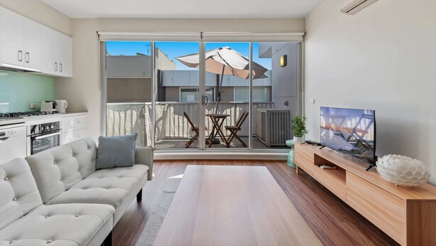 A modern living room with a sofa, TV, and wooden entertainment unit. - Stylish North Melbourne Stay (Melbourne)