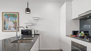 A modern kitchen with a stainless steel sink, white cabinets, and a black pendant light. - A Taste of Paradise in Inner City Suburbia (Melbourne)