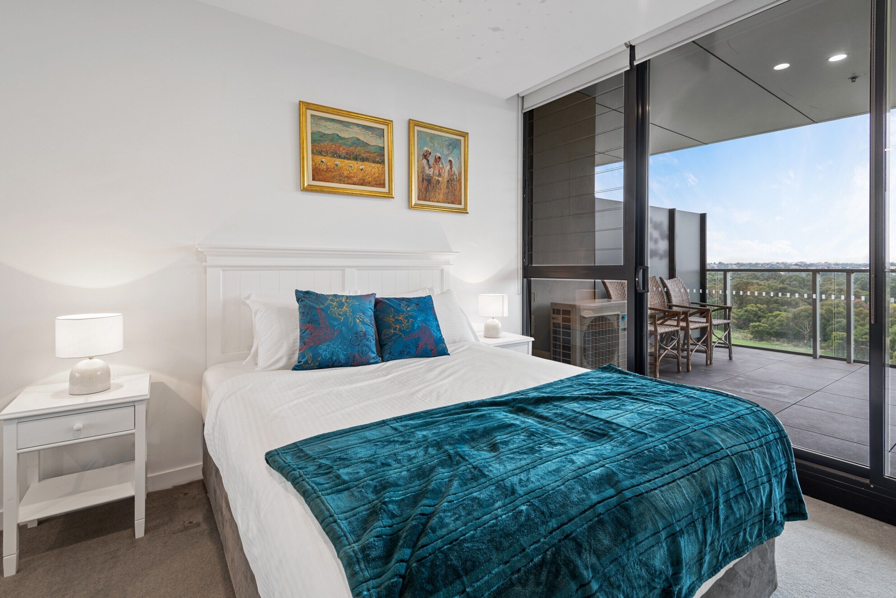 A modern bedroom with a large bed, white nightstands, and a balcony with a view.