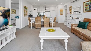 A modern living room with a white coffee table, wicker chairs, a brown leather sofa, and a dining area with wicker chairs and a white table. - A Taste of Paradise in Inner City Suburbia (Melbourne)