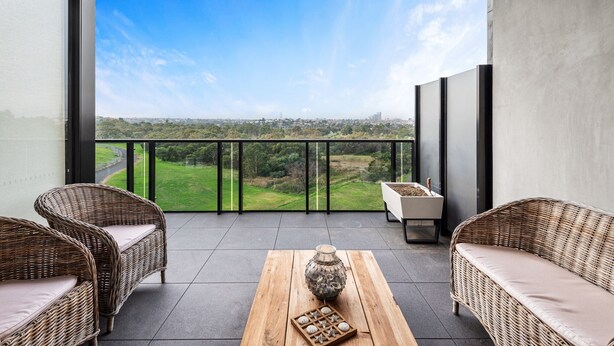 A balcony with wicker furniture, a wooden table, and a view of a green landscape. - A Taste of Paradise in Inner City Suburbia (Melbourne)
