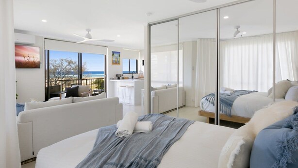 A modern hotel room with a large bed, a balcony with a view of the sea, and a separate sitting area with a view of the ocean. - Beachfront Studio With Balcony & Stunning Views (Gold Coast)