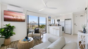 A modern living room with a sofa, a coffee table, and a view of the kitchen and balcony. - Beachfront Studio With Balcony & Stunning Views (Gold Coast)
