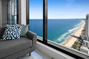 A modern living room with a large window overlooking a beach and high-rise buildings. - Oceanfront 2-bed With Spectacular View Pool & Gym (Gold Coast)