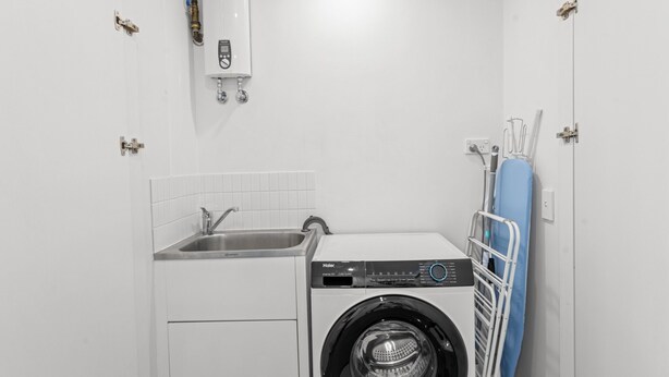 A compact laundry room with a front-loading washer and a sink. - Stylish West End Stay With Rooftop Pool & BBQ (Brisbane)