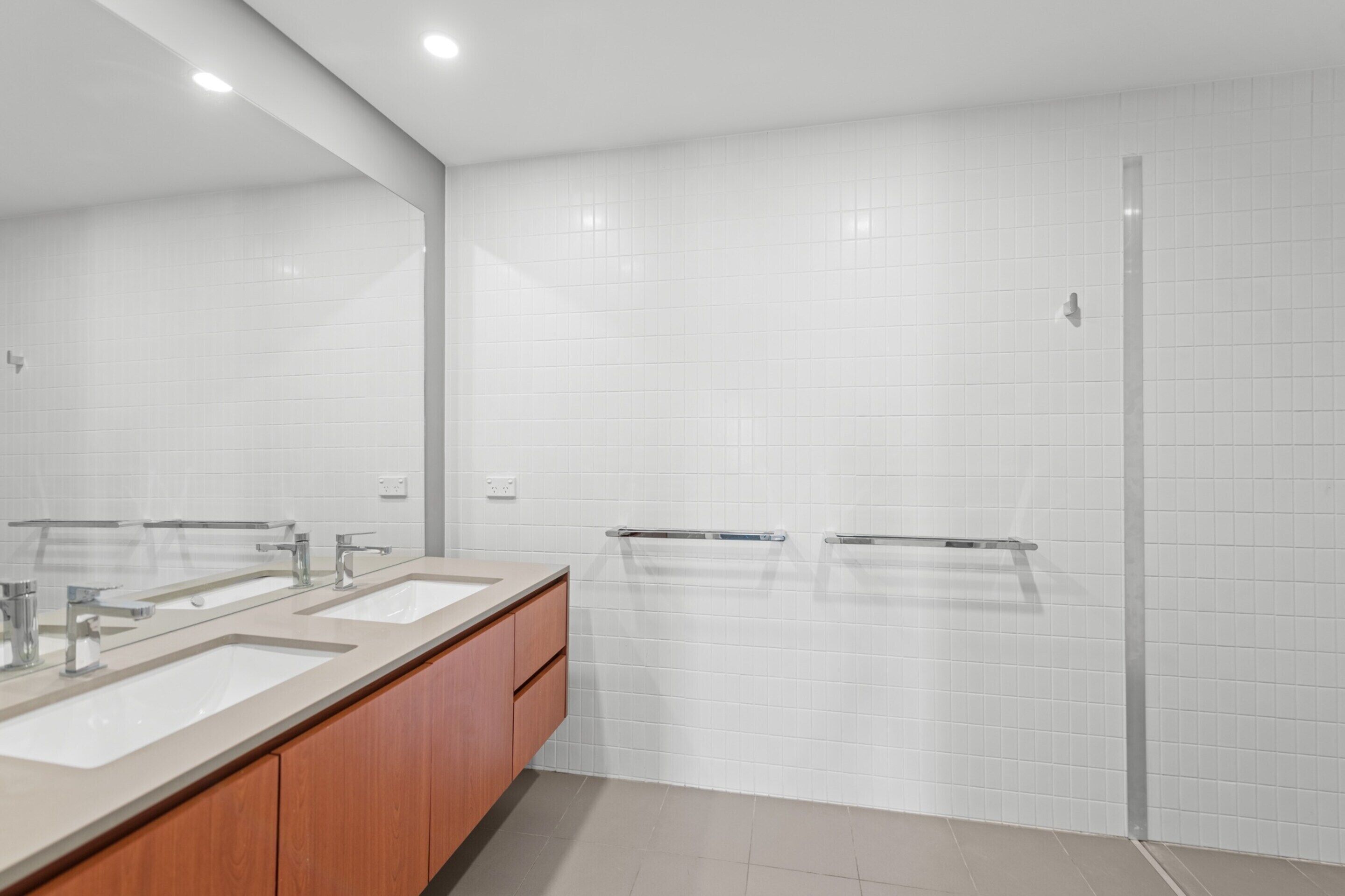 Un baño moderno con tres lavamanos, armarios de madera y cabina de ducha de vidrio.